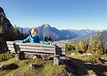 Frau mit leichtem Rheuma ruht sich bei Wanderung auf einer Bank aus. 