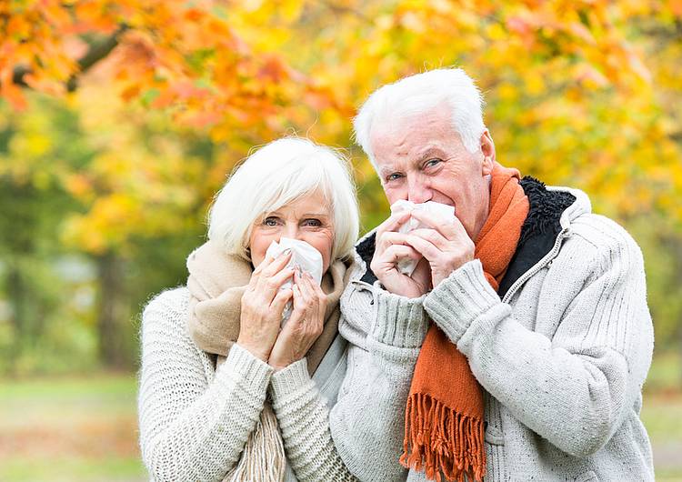 Älteres Paar putzt sich bei Herbstspaziergang zur Grippeimpfung  die Nase. 