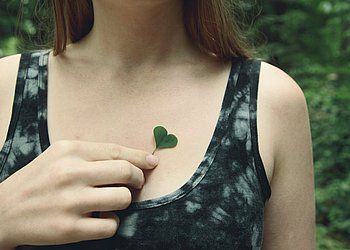 Das Foto zeigt eine Hand, die ein grünes herzförmiges Kleeblatt auf die Haut am Brustbein legt.