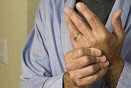 Ein Mann massiert sich die Hände, die aufgrund einer Autoimmunkrankheit schmerzen. 