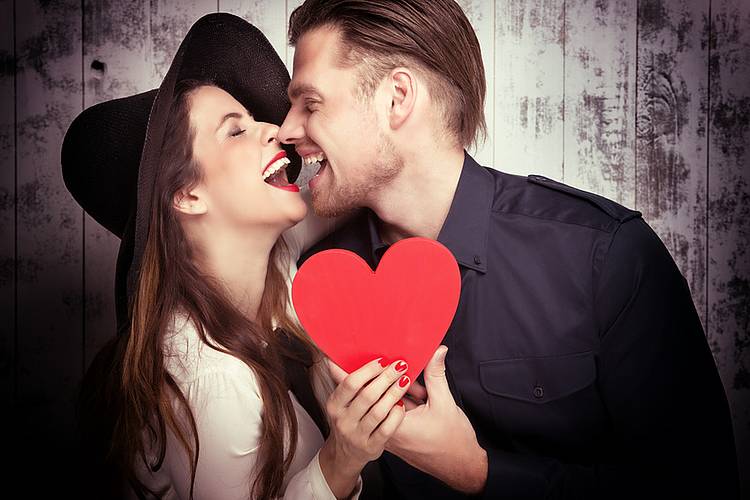Frau und Mann mit rotem Herz in den Händen lachen sich an.