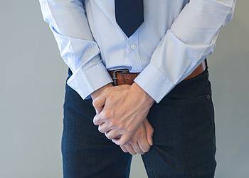 Mann in Anzug hält sich gefaltete Hände vor die Prostata.