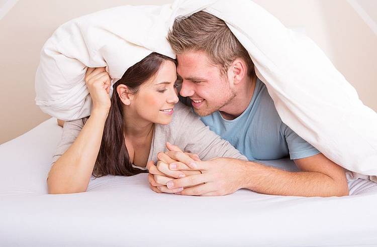 Junges Paar unter einer Decke hält Händchen 