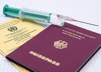 Impfpass, Reisepass und Impfspritze liegen übereinander.