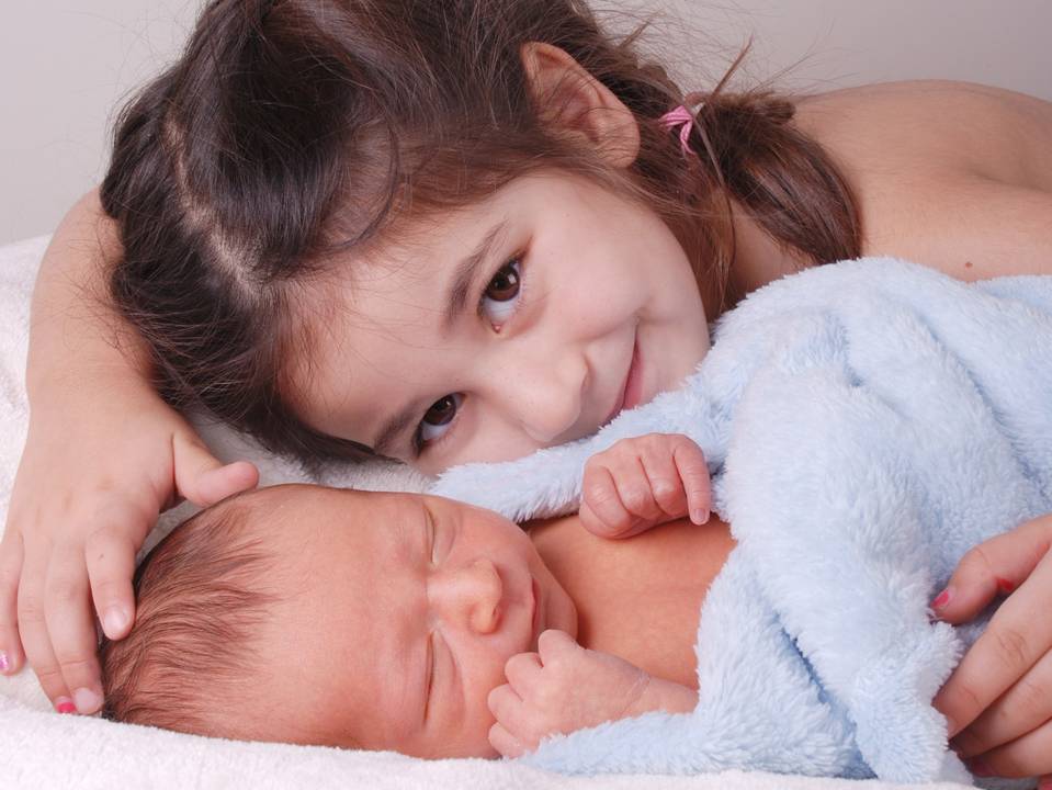 Kleines Mädchen umarmt neugeborenes Baby. 