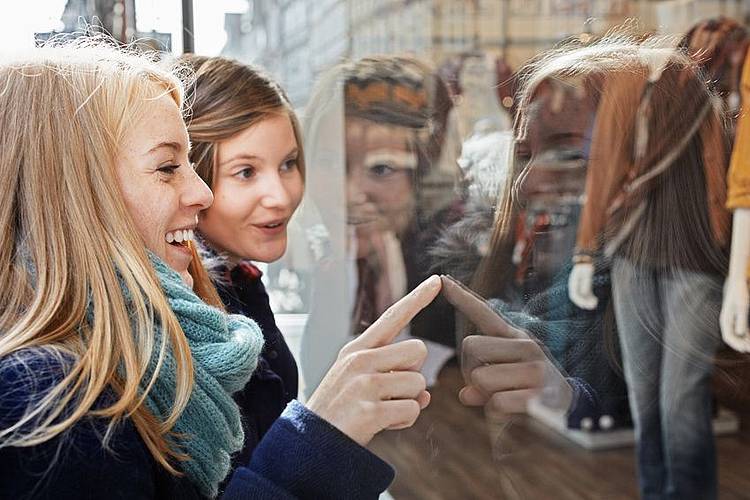 Junge Frauen zeigen mit blassen, kalten Fingern auf die Auslage in einem Schaufenster.
