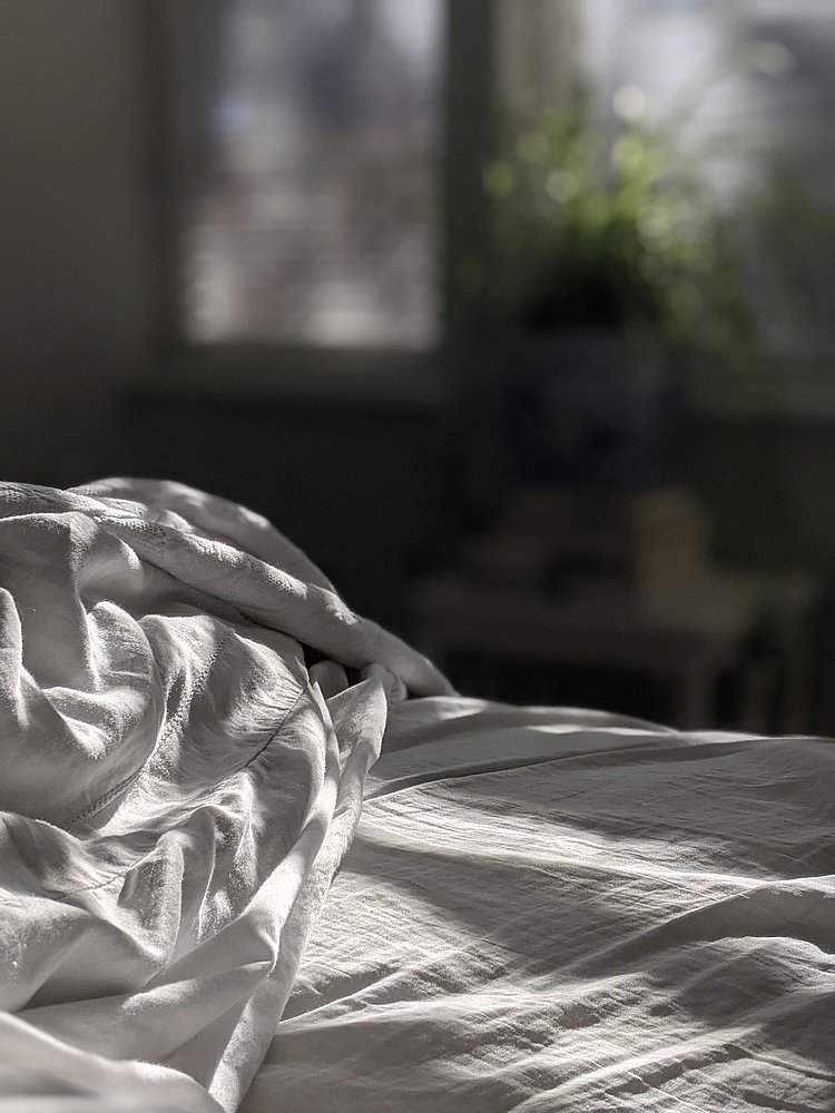 Das Foto zeigt ein zerwühltes Bett, auf das die Sonne scheint.