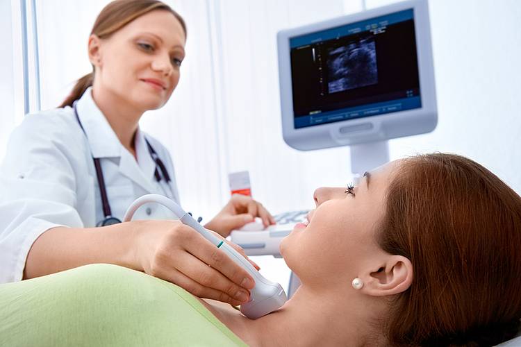 Ärztin untersucht Schilddrüse einer Patientin mit Ultraschall. 