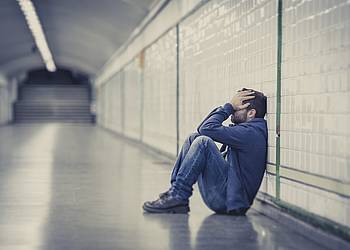 Junger Mann mit psychischer Erkrankung sitzt verzweifelt an einem U-Bahnsteig.