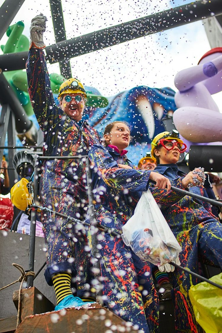 Feiernde Menschen fahren auf einem Karnevals-Wagen durch Konfetti-Regen 