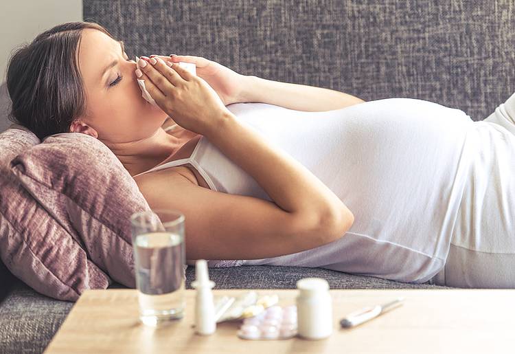 Schwangere Frau liegt mit Erkältung auf dem Sofa